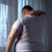 Obese man stretching neck muscles, back pain problems caused by overweight