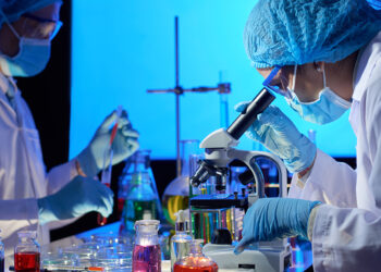 Team of scientists working on covid-19 vaccine in dark laboratory, mixing liquids and looking through microscope