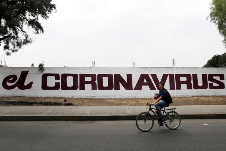 A coronavirus sign is seen on the wall as a man passes on a bicycle as the coronavirus disease (COVID-19) continues in Mexico City