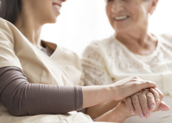 Close-up of person touching hand of senior woman. Caregiving in the nursing home