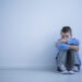Alienated boy sitting alone on floor against wall with copy space. Sad child with autism concept