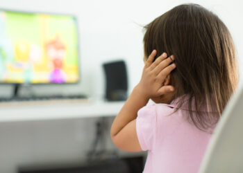 A child watching tv holding her ears because she is afraid of the sound; Child behavior theme