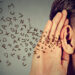 man holds his hand near ear and listens carefully alphabet letters flying in isolated on gray wall background